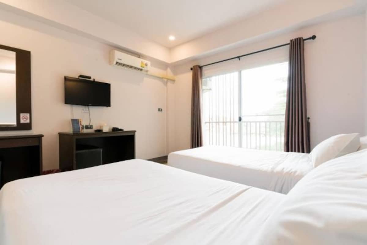 Habitación de hotel con dos camas, televisor, escritorio y ventana con cortinas.
