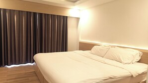 A neatly made bed with white linens in a hotel room with wooden flooring and a large window with curtains. - Smile Place Hotel Chiang Rai (Chiang Rai)