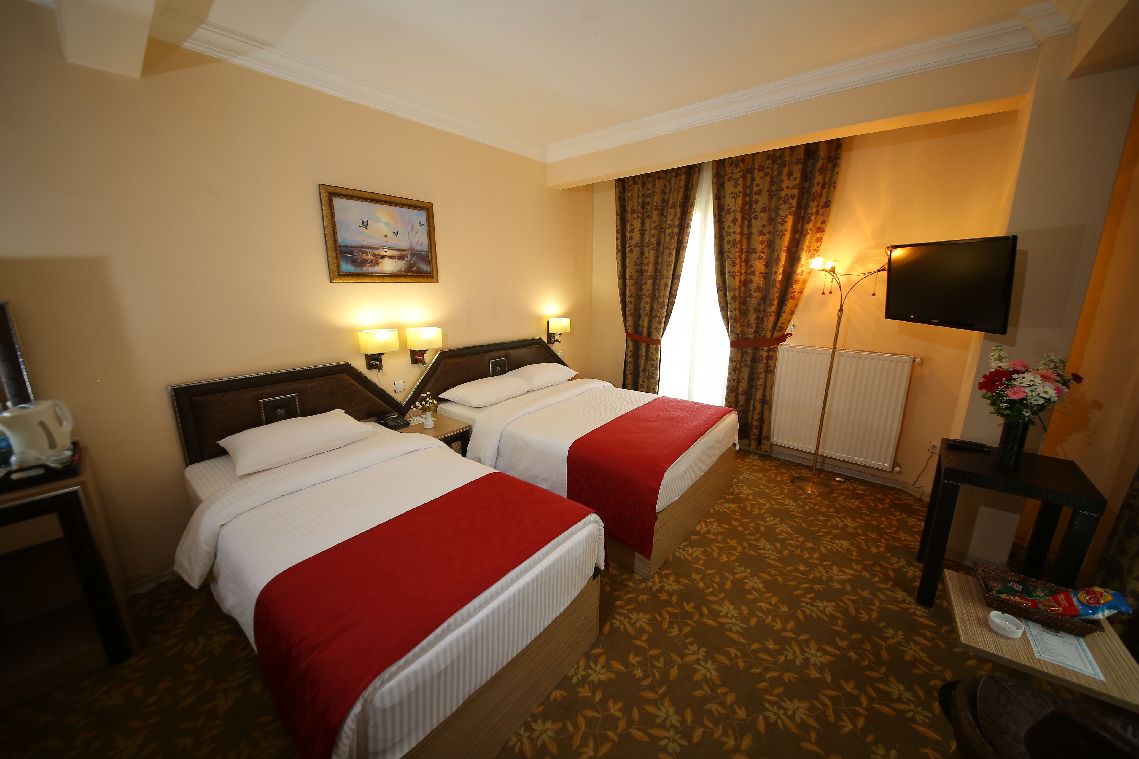 A hotel room with two beds, a television, a desk with a lamp, and a painting on the wall.