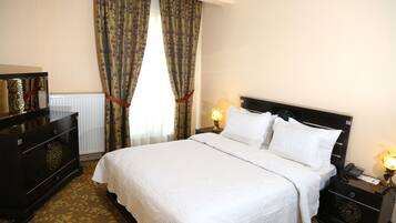 Een hotelkamer met een groot bed, een dressoir, een nachtkastje met een lamp en gordijnen.