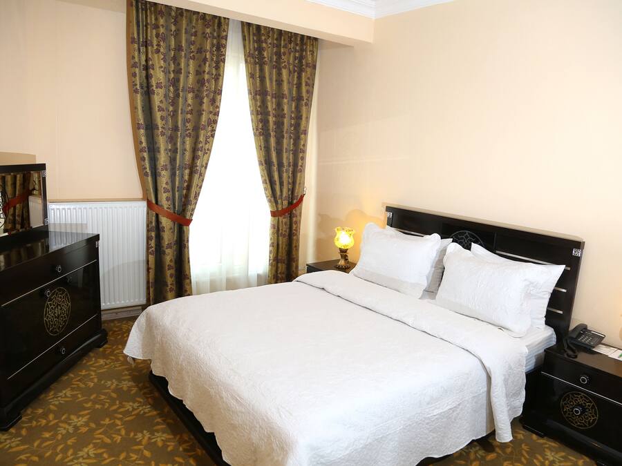 Een hotelkamer met een groot bed, een dressoir, een nachtkastje met een lamp en gordijnen.