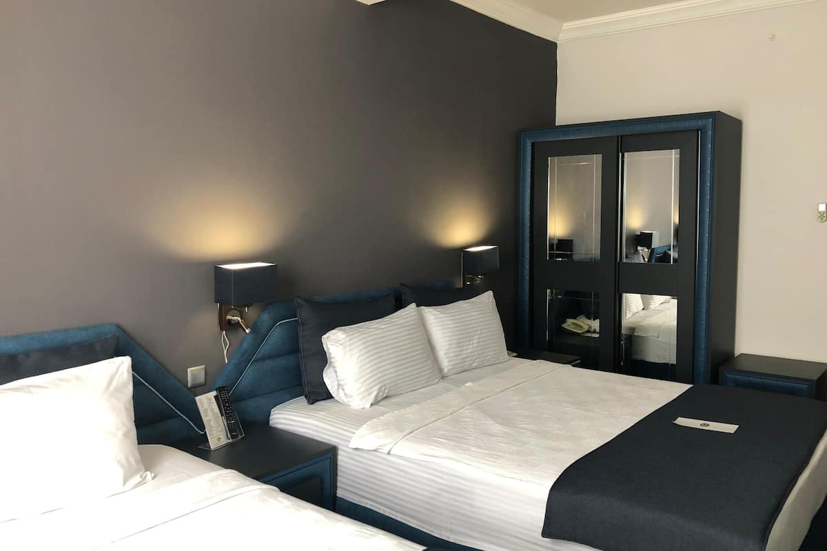Hotellihuone, jossa on suuri sänky, yöpöytä lampun kanssa, vaatekaappi ja peili.