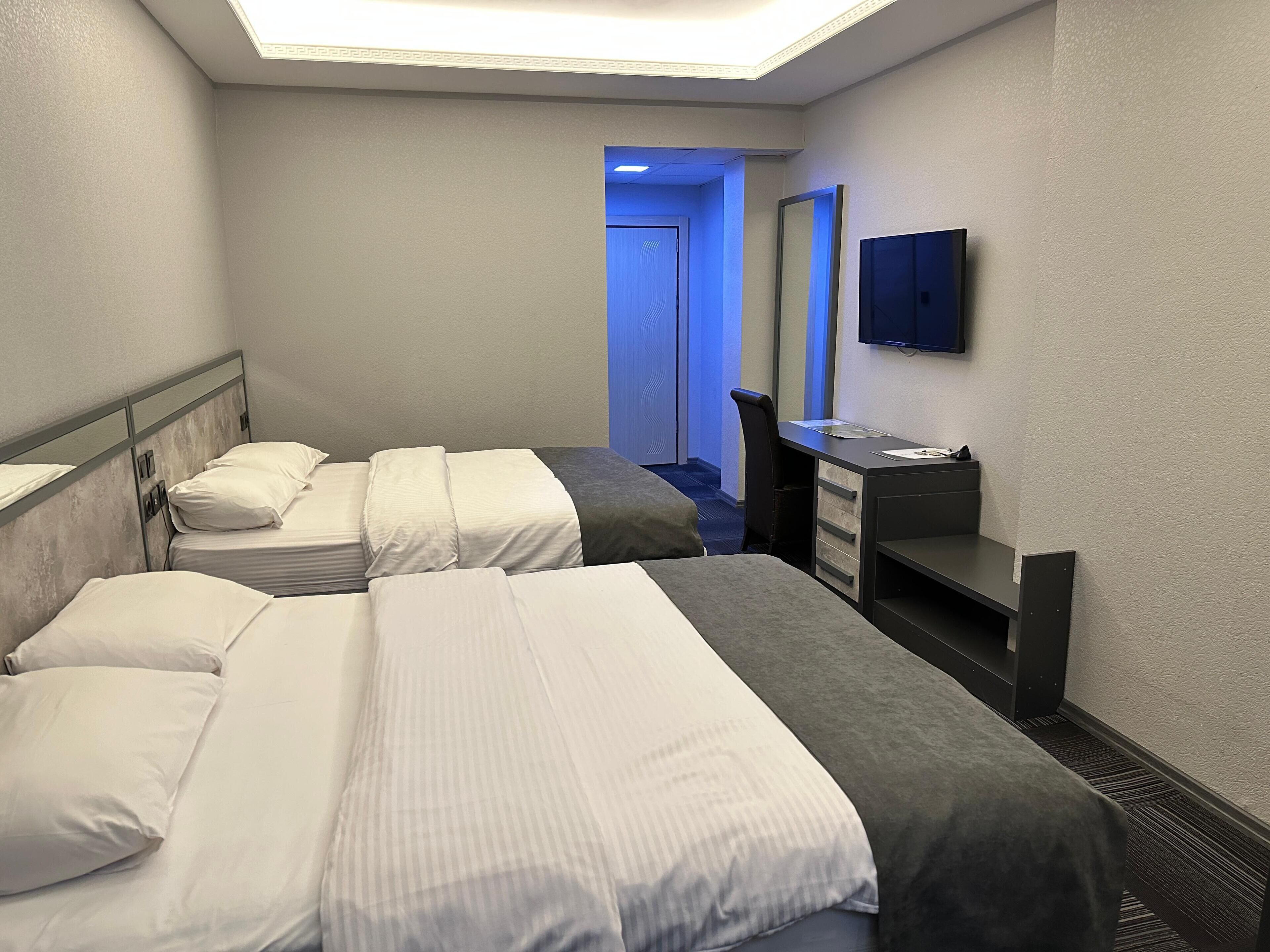 Une chambre d’hôtel avec deux lits, un bureau, une chaise, une télévision et une porte donnant sur une salle de bain.