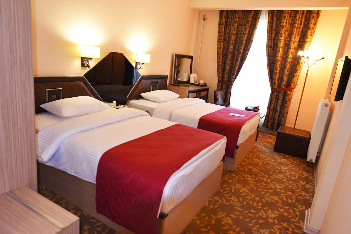 Hotellihuone, jossa on kaksi sänkyä, yöpöytä, lamppu, peili ja ikkuna, jossa on verhot.