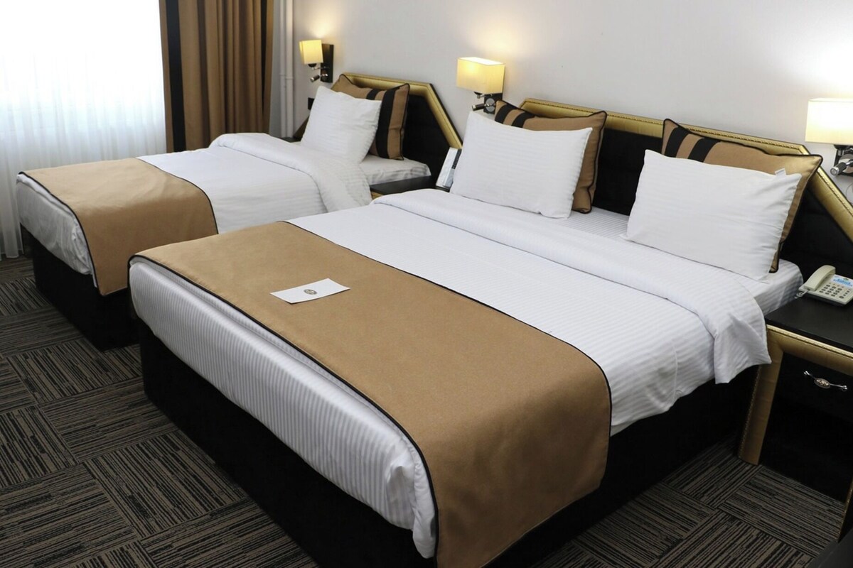 Ein Hotelzimmer mit zwei Betten, einem Nachttisch mit Telefon und einem Fenster mit Vorhängen.