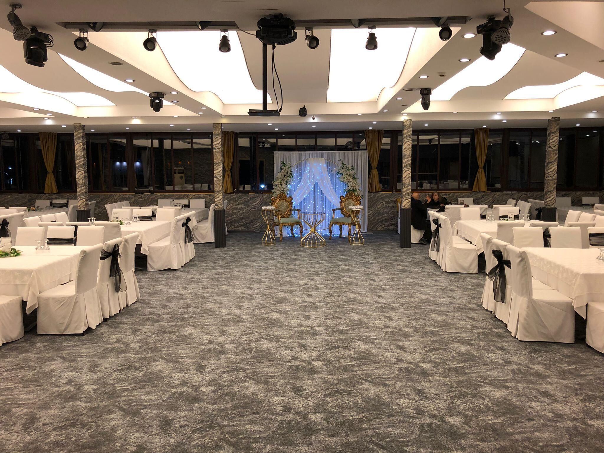 A banquet hall with rows of tables and chairs, a stage with a backdrop, and a ceiling with recessed lighting.
