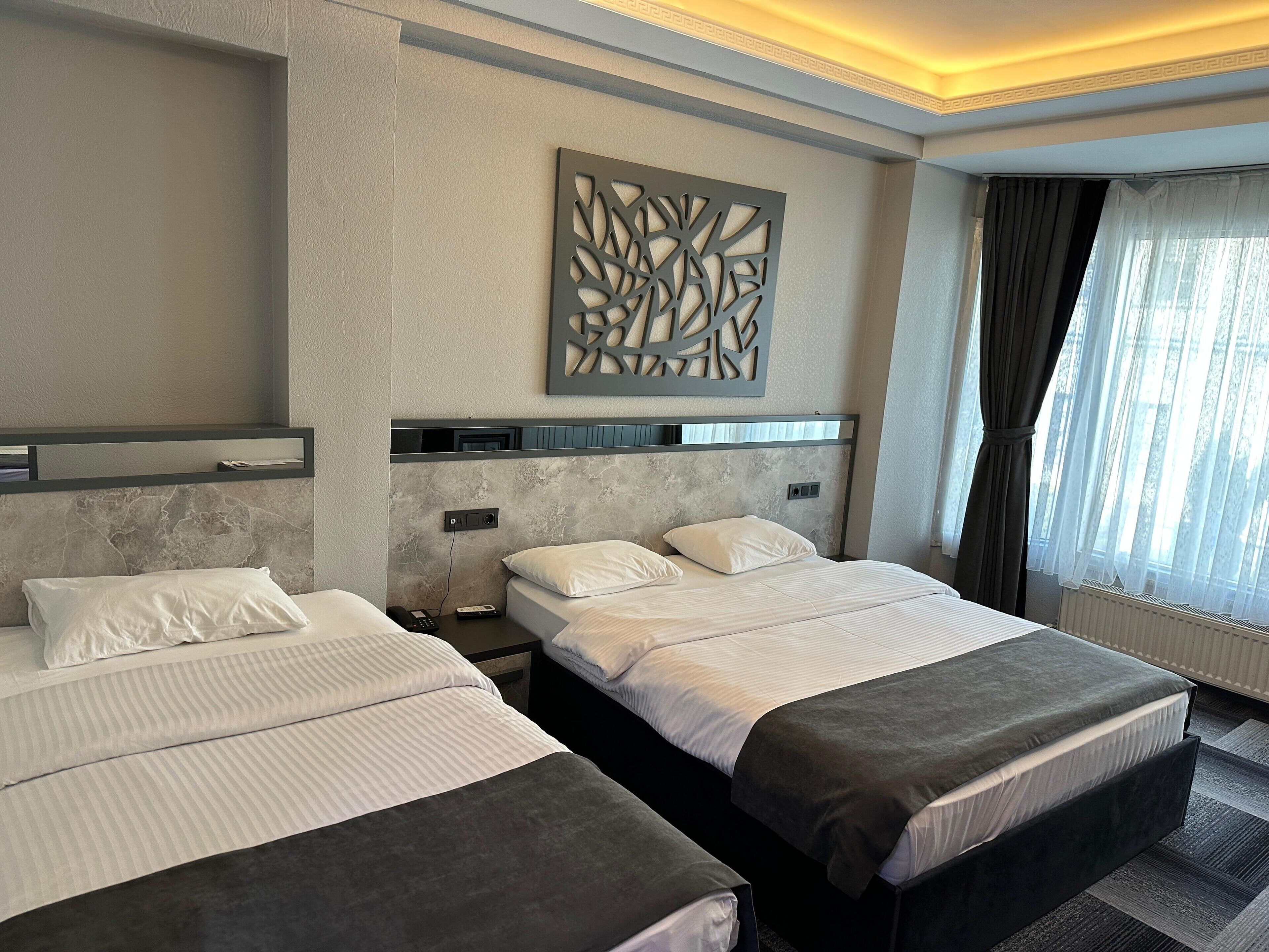 A hotel room with two beds, a modern headboard, a decorative wall piece, and a window with curtains.