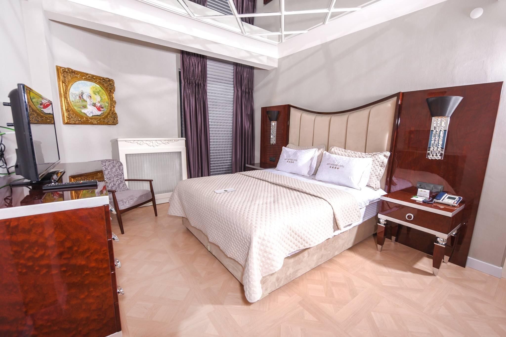 A bedroom with a bed, bedside table, desk, chair, and a television.