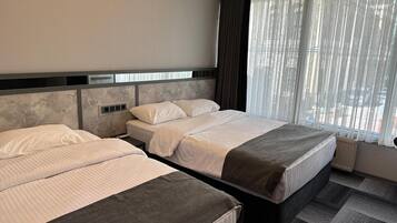 Een hotelkamer met twee bedden, een groot raam met dunne gordijnen, en een modern hoofdeinde.