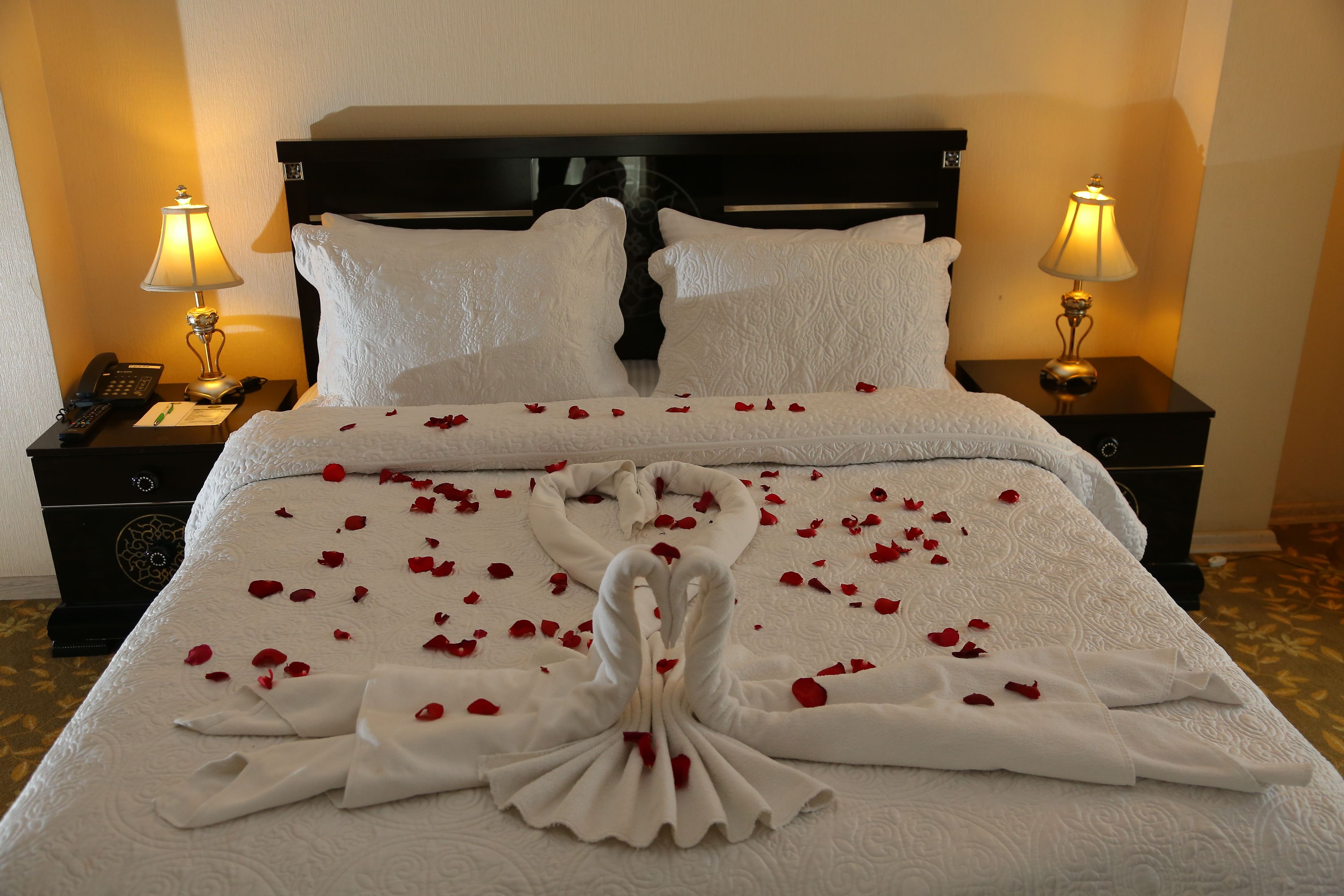A hotel room with a neatly made bed, two bedside lamps, a telephone, and a nightstand with a clock.