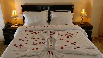 A hotel room with a neatly made bed, two bedside lamps, a telephone, and a nightstand with a clock.