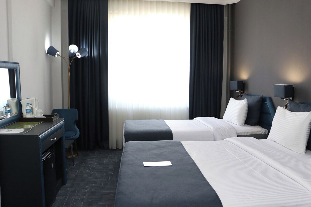 A hotel room with two beds, a desk, a chair, a mirror, and a window with curtains.