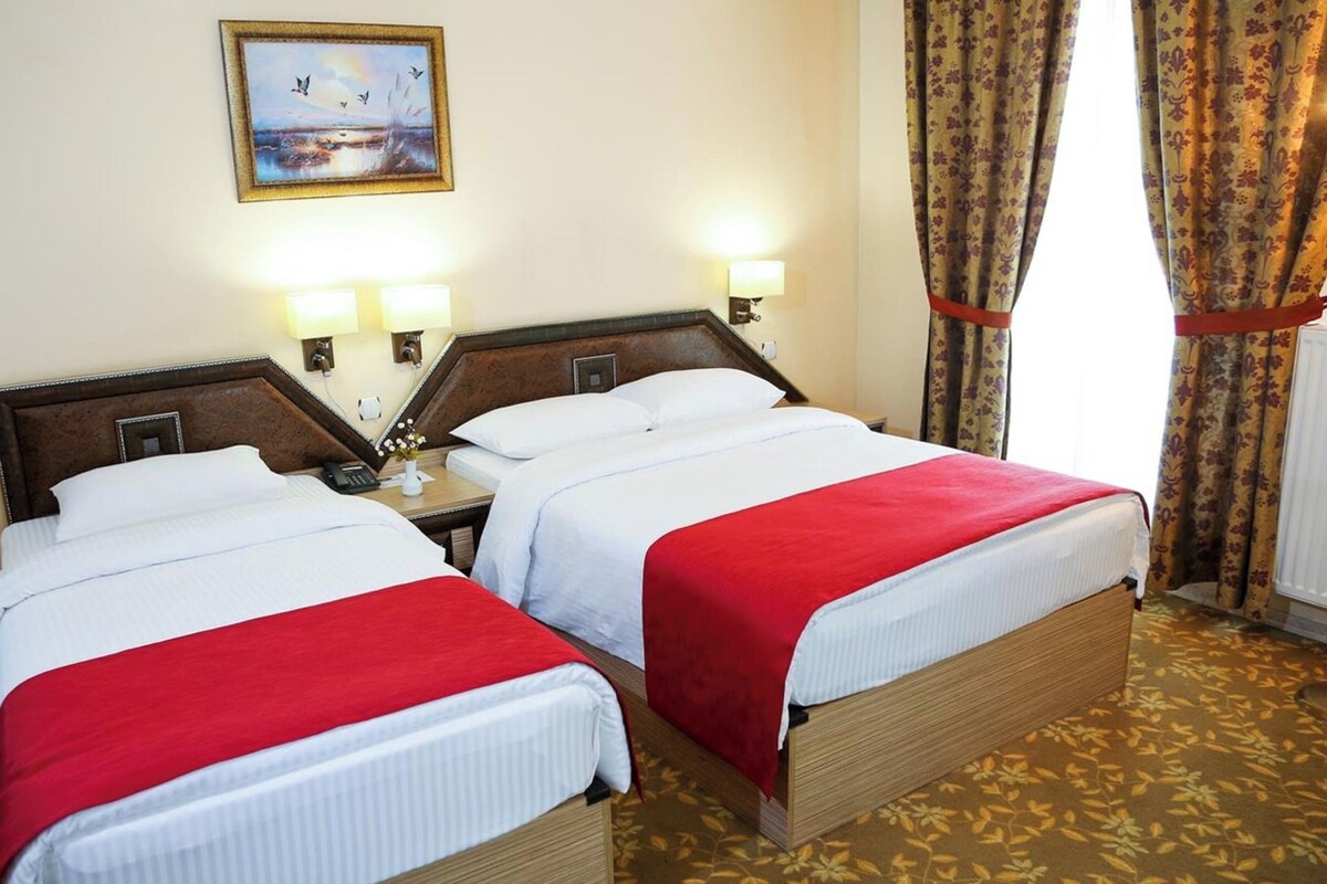 A hotel room with two beds, a nightstand with a phone, and a painting on the wall.