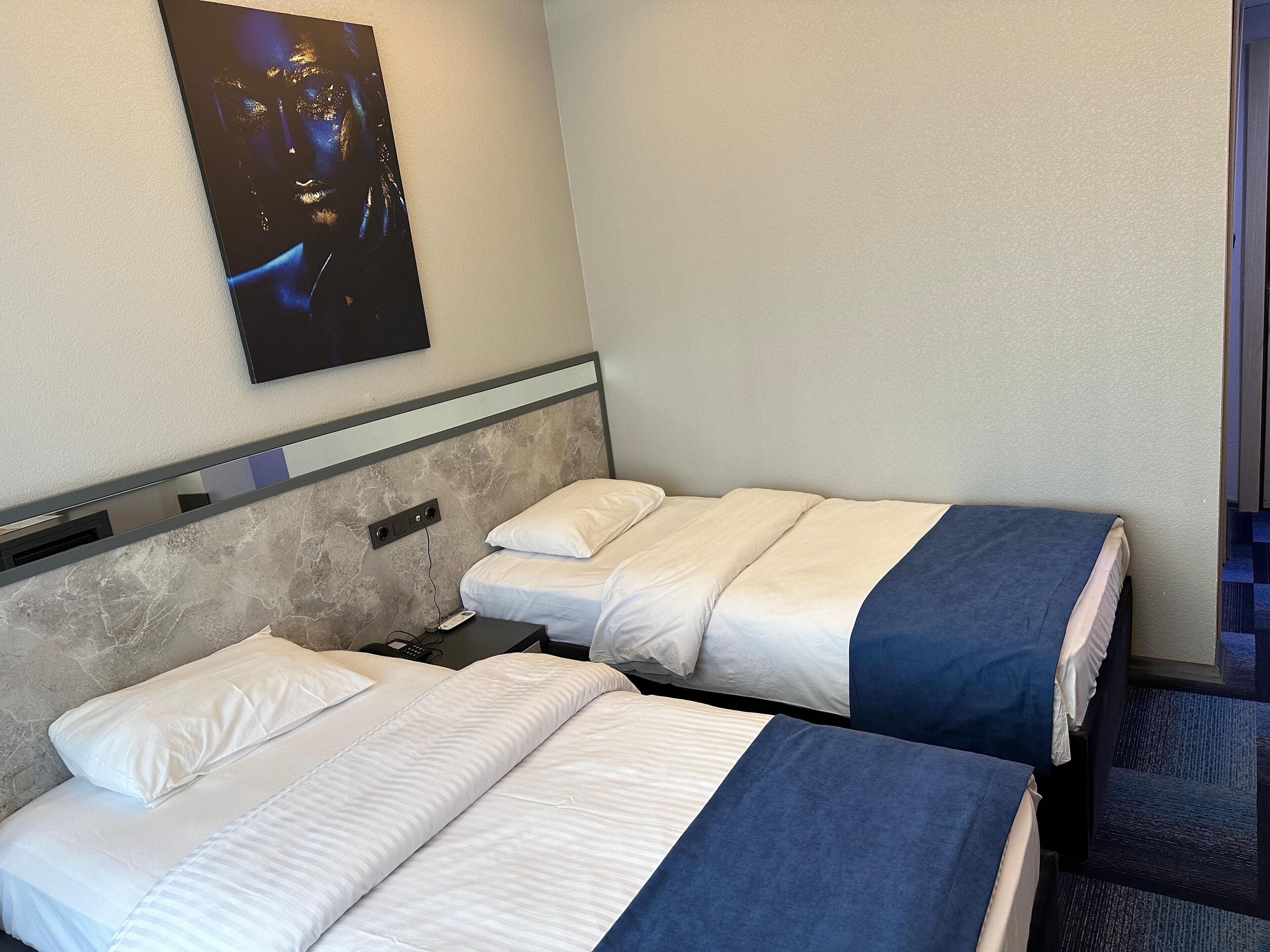 Una habitación de hotel con dos camas individuales, cabecera de mármol, televisor montado en la pared y suelo alfombrado.
