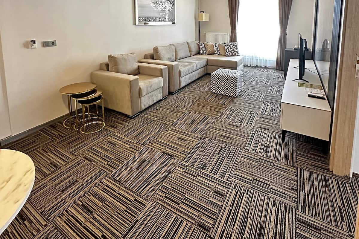 Hotellihuoneessa on sohvaryhmä, pieni pyöreä pöytä, kuviollinen matto, kattovalaisin ja suuri peili.