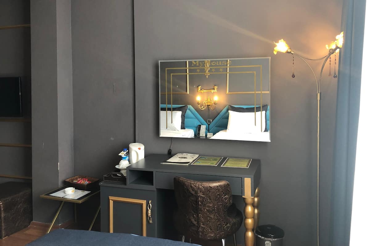 Moderni hotellihuone, jossa on suuri sänky, työpöytä tietokoneella, pieni pöytä ja kori sekä seinälle asennettu televisio.