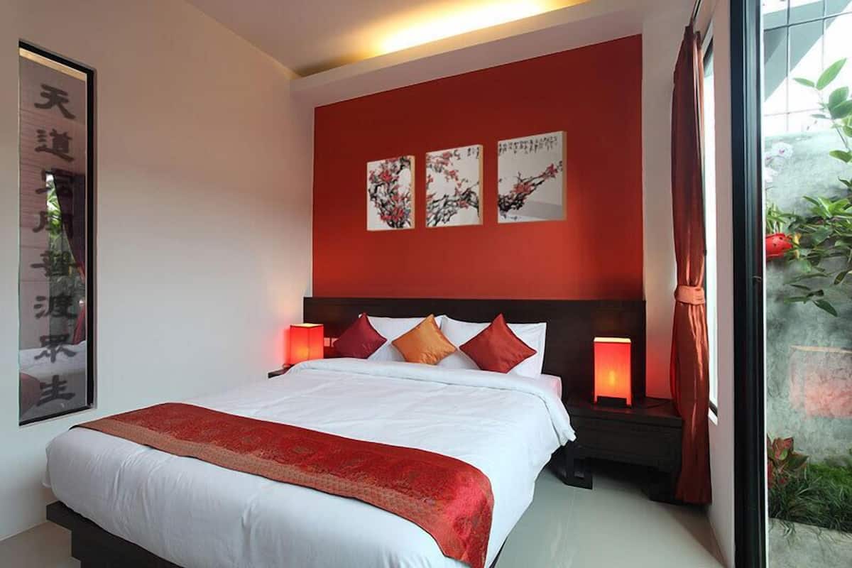 Un dormitorio con una cama grande, paredes de acento rojas y tres obras de arte enmarcadas sobre la cama.