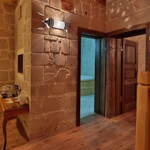 Paredes de pedra rústicas, mesa e cadeiras de madeira, uma porta de madeira e vista para um quarto com uma banheira.