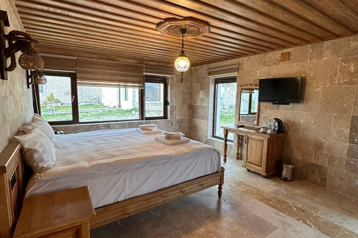 Un dormitorio espacioso con una cama grande, techo de madera, paredes de piedra, televisión y vistas al exterior.