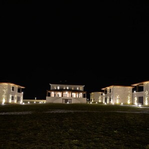 Um edifício grande, com vários andares e fachada simétrica, iluminado por luzes no chão.