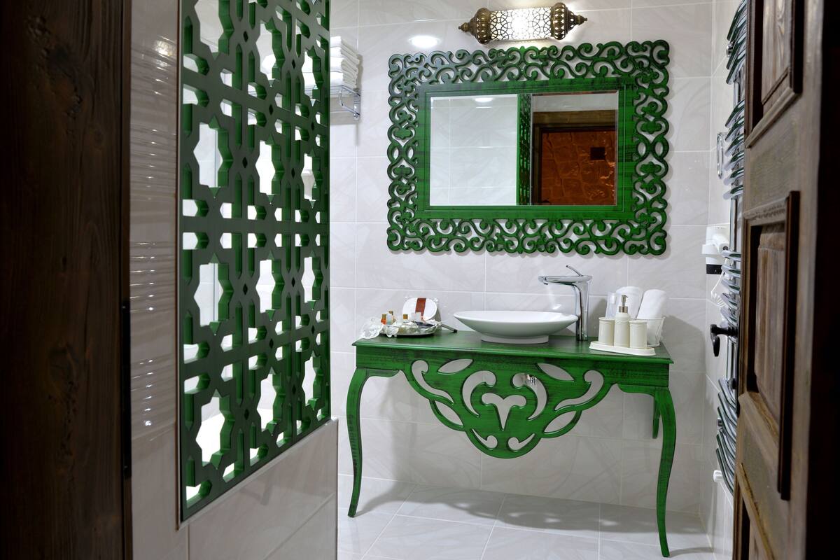 Un baño con tocador verde, baldosas blancas, un espejo grande y un separador decorativo.