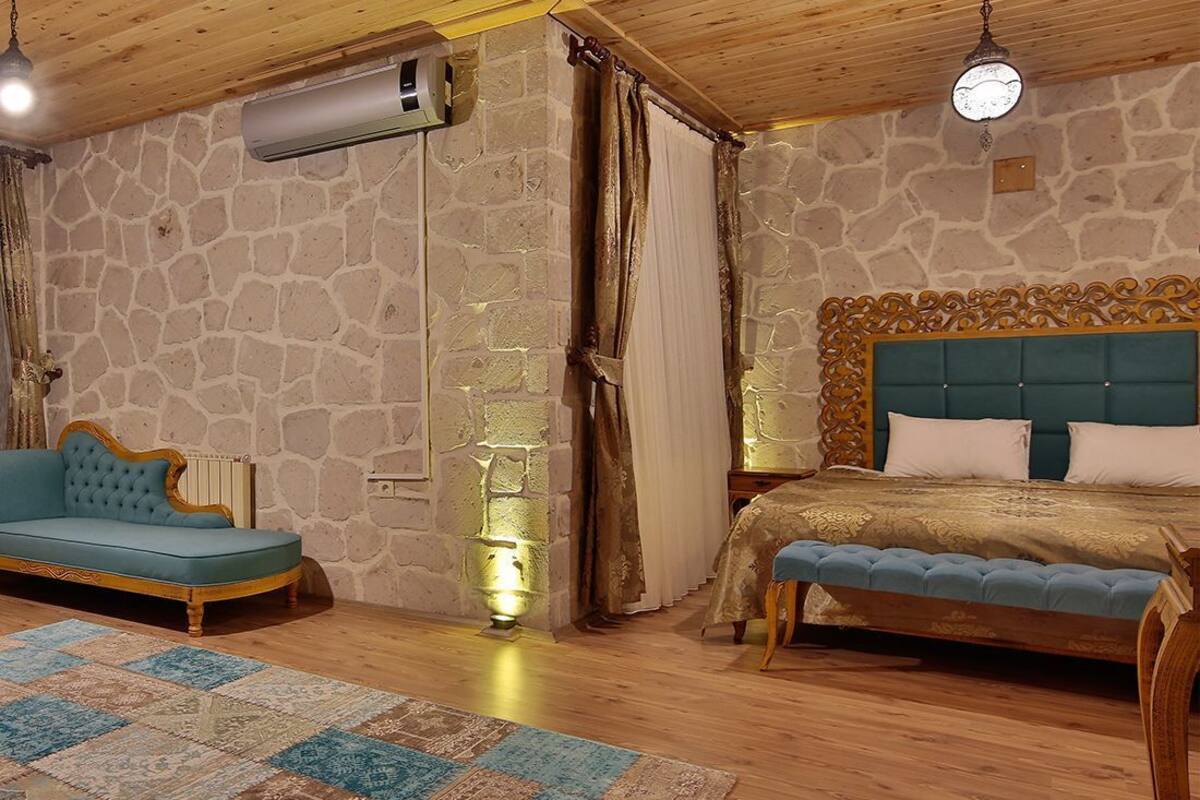 Una habitación con pared de piedra, techo de madera, cama con cabecera azul, sofá azul y alfombra estampada.