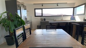 Une cuisine moderne avec un coin repas, de grandes fenêtres et une plante en pot.
