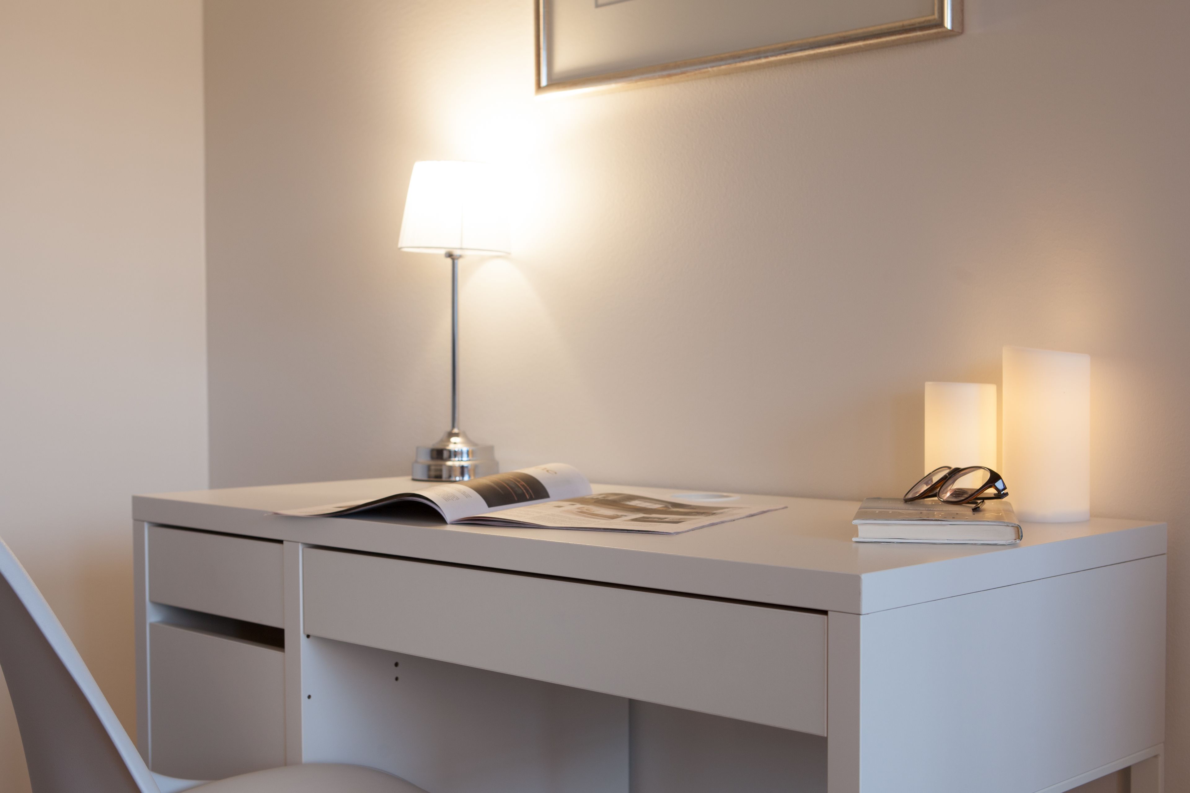 Een modern, minimalistisch bureau met een lamp, een boek en een bril.