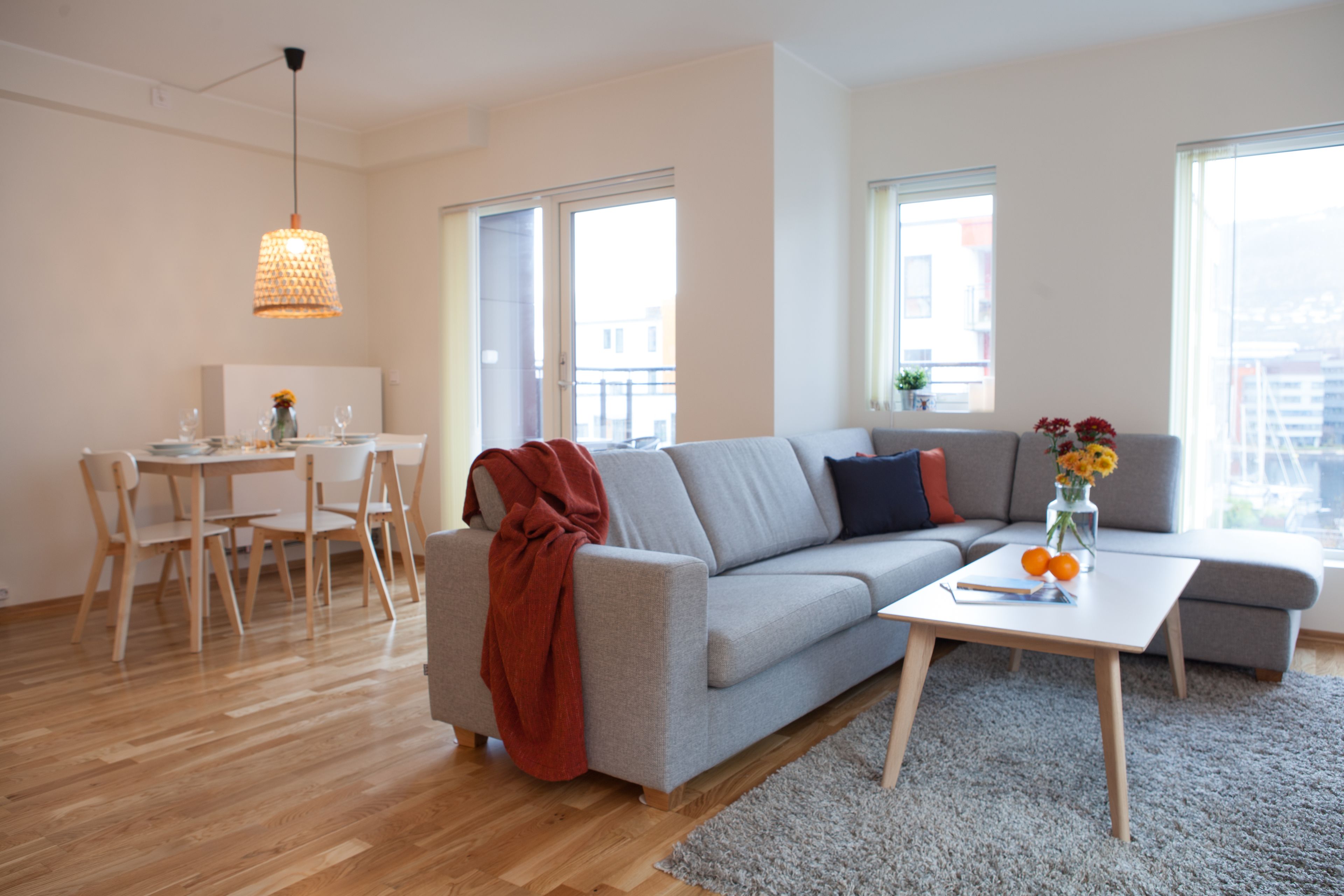 A modern living room with a grey sofa, a coffee table, and a dining area with wooden chairs.