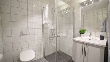 Un baño moderno con ducha envuelta en vidrio, inodoro blanco y lavabo con espejo superior.