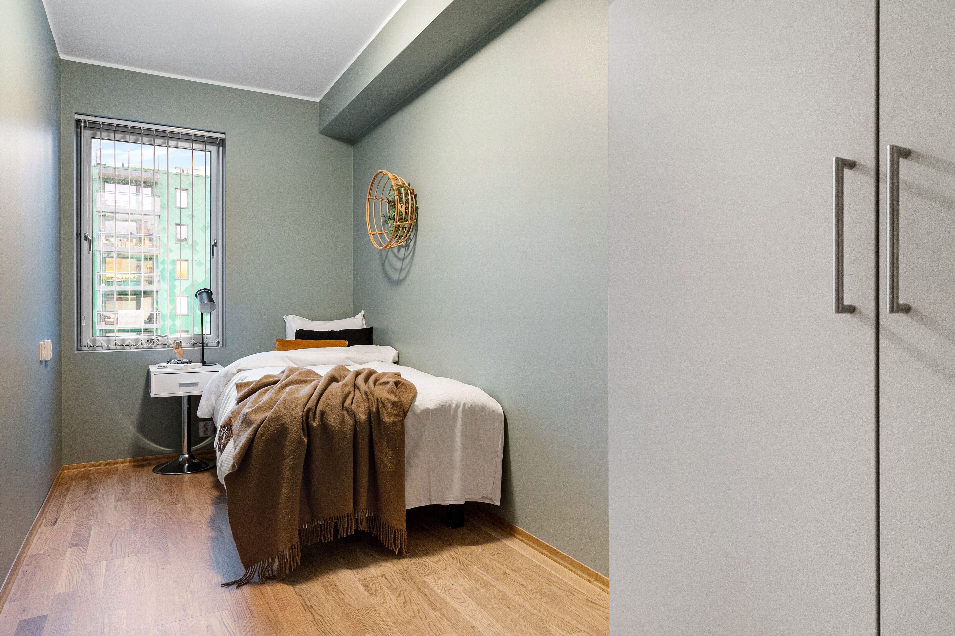 Un dormitorio con cama, mesita de noche, lámpara, ventana con persianas y un adorno en la pared.
