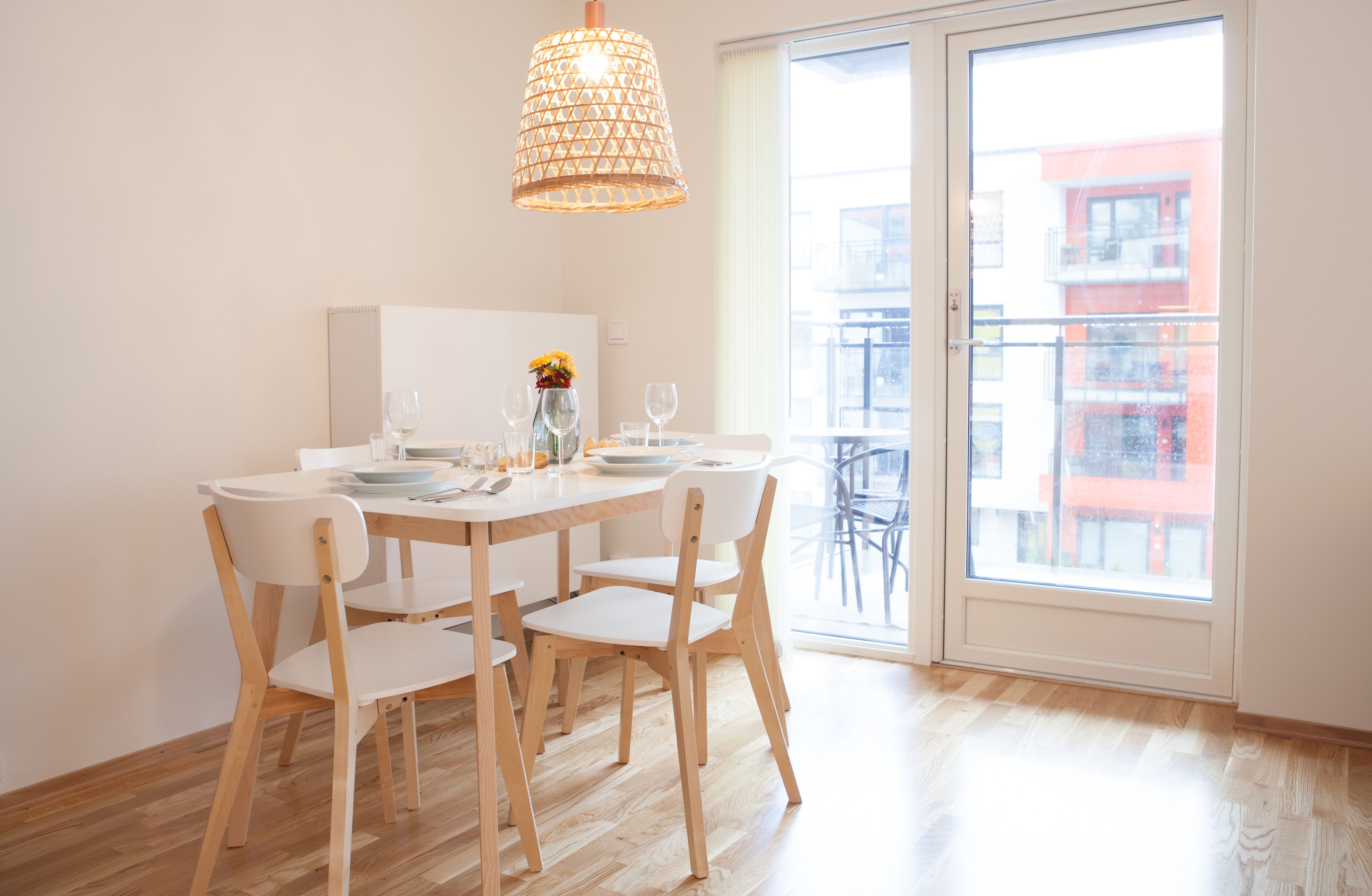 A dining area with a wooden table and chairs, a hanging light fixture, and a view of a building through a glass door.