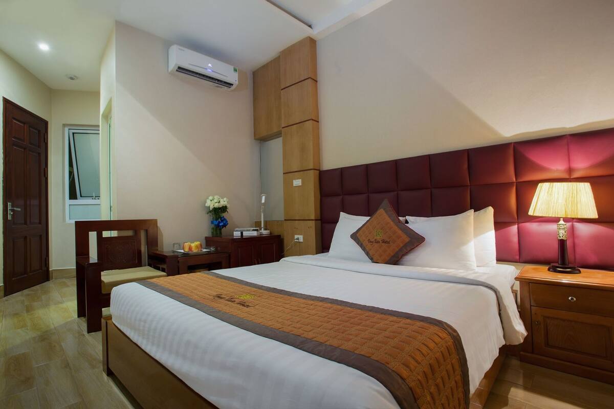 Habitación de hotel con cama, mesita de noche, lámpara y aire acondicionado.