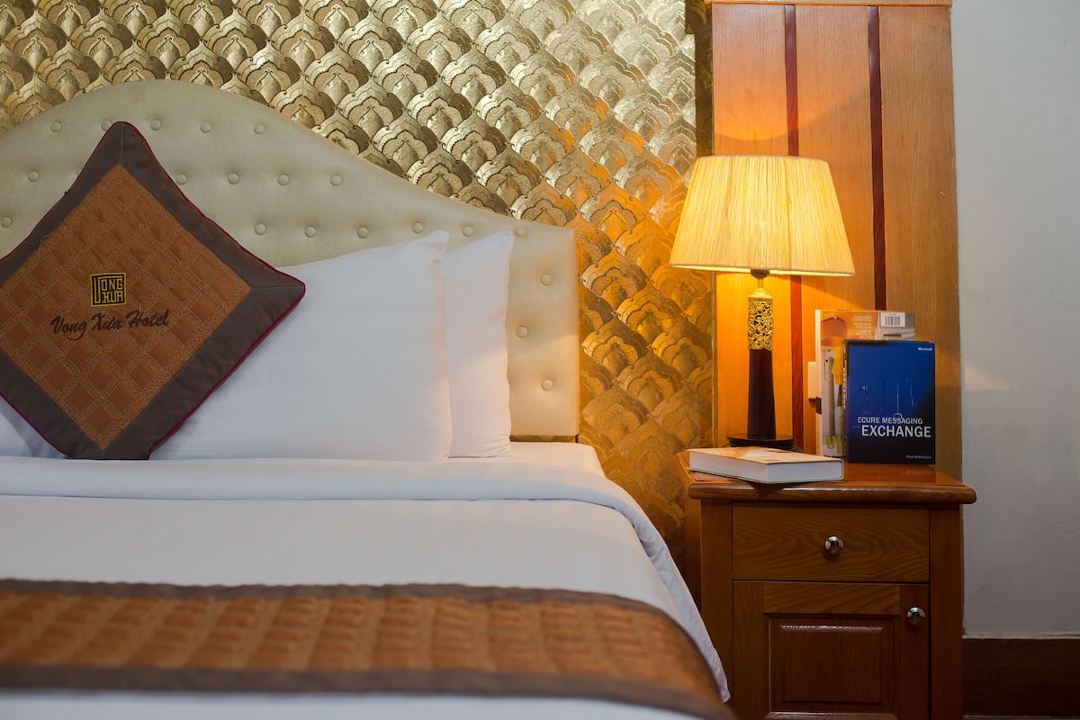 Una habitación de hotel con una cama bien hecha, una mesita de noche con una lámpara y un libro titulado 'EUREC Messaging Exchange'.