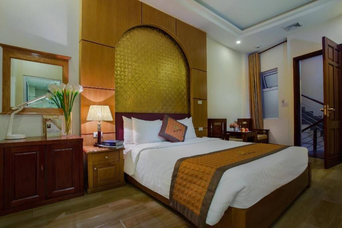 Habitación de hotel con una cama grande, cabecera de madera, un escritorio con lámpara, un espejo y vistas a una escalera.