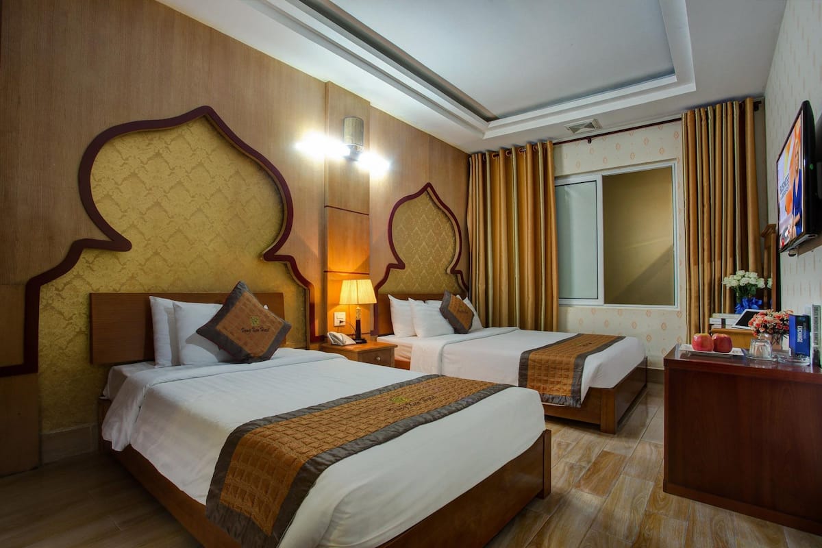 Habitación de hotel con dos camas, cabeceros de madera, un escritorio con televisor y una ventana con cortinas.