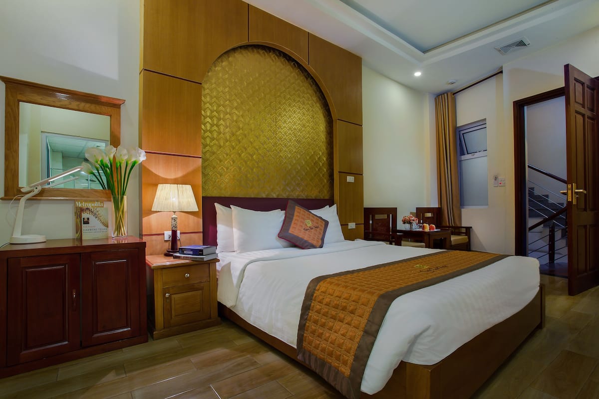Habitación de hotel con una cama grande, cabecero de madera, un escritorio con lámpara, un espejo y vistas al exterior.