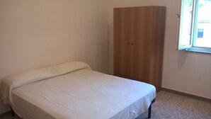 Une chambre avec un lit simple, une armoire en bois et une fenêtre.