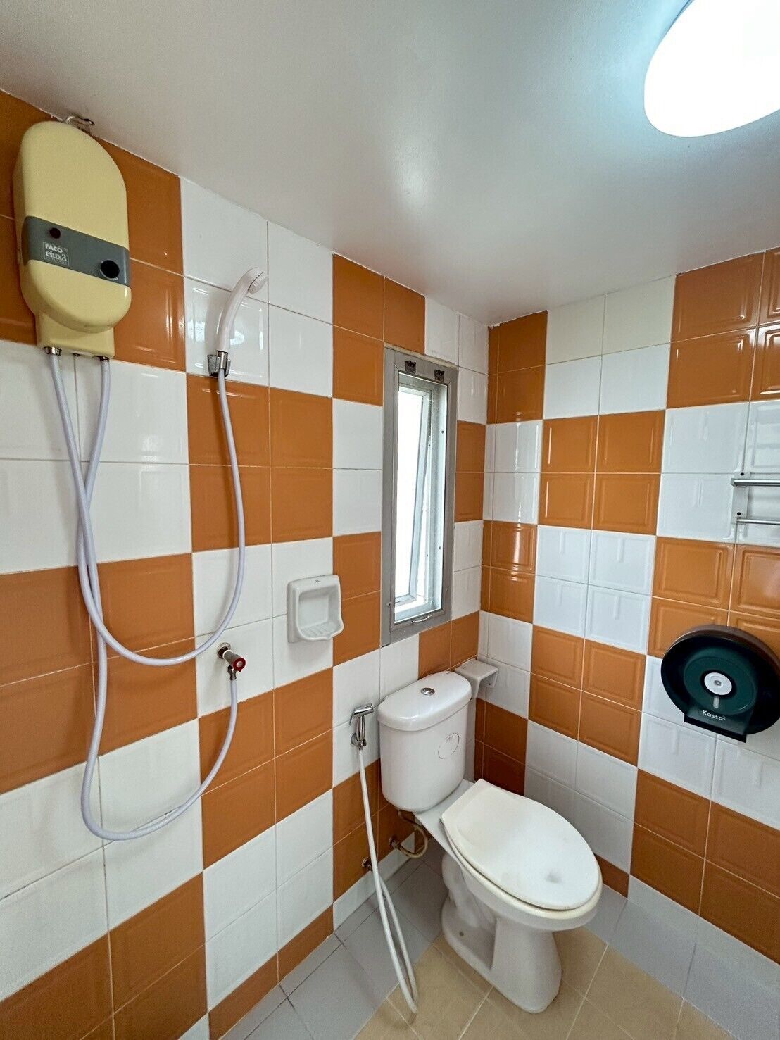 A bathroom with orange and white checkered tiles, a toilet, a sink with a soap dispenser, and a shower head.