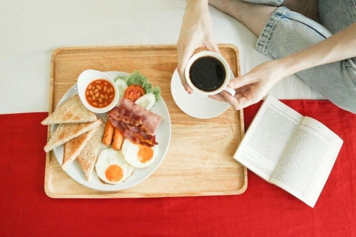 A breakfast tray with toast, eggs, bacon, beans, and tomatoes on a wooden tray.