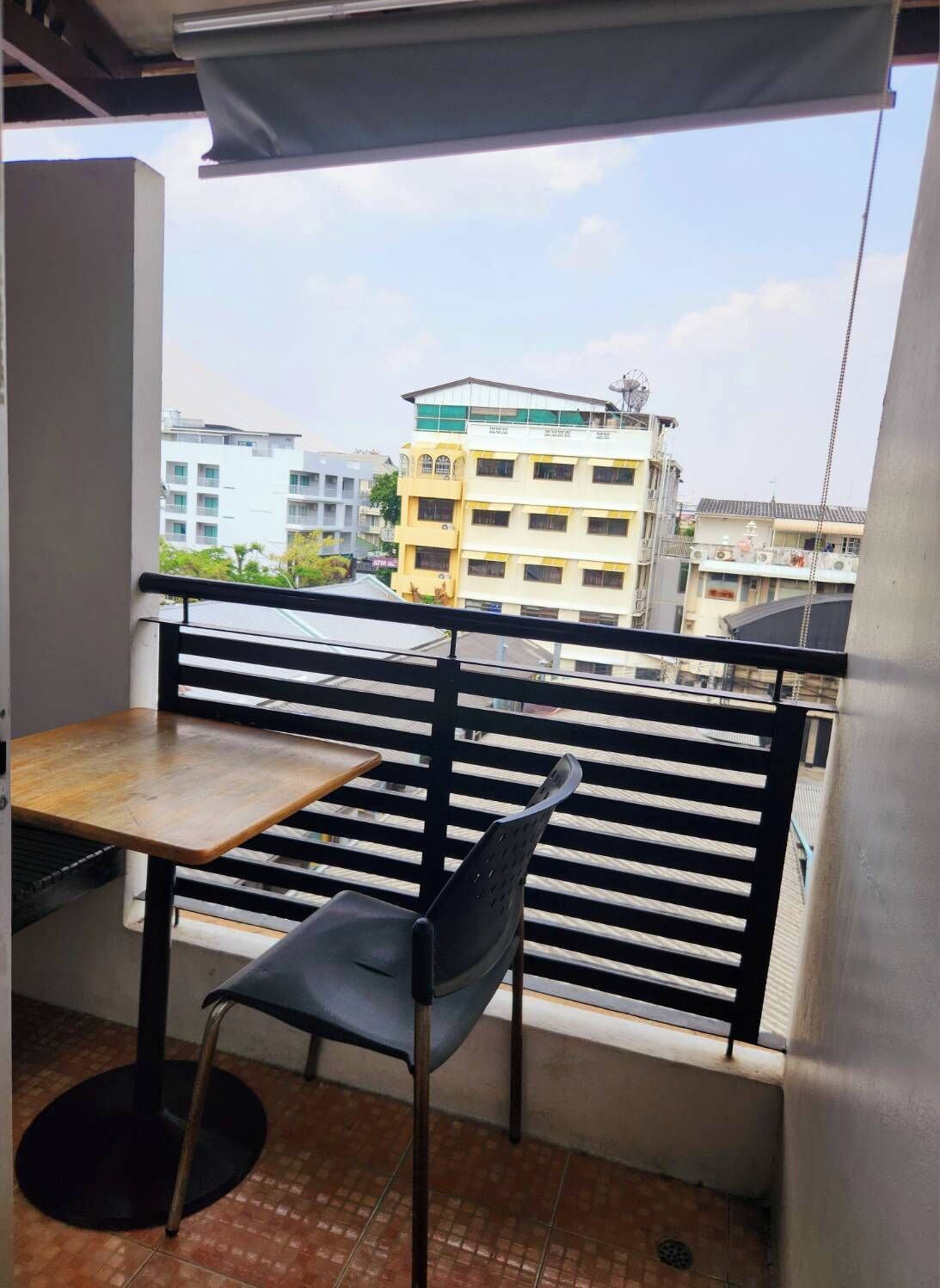 Ein Balkon mit Tisch und Stuhl, einem Metallgeländer und Blick auf Gebäude im Hintergrund.