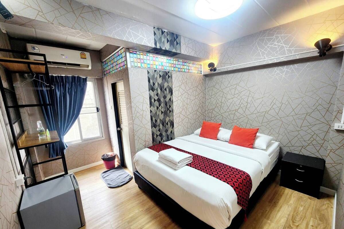 Une chambre d’hôtel moderne équipée d’un lit, d’un petit bureau, d’un radiateur et d’une fenêtre avec des rideaux.