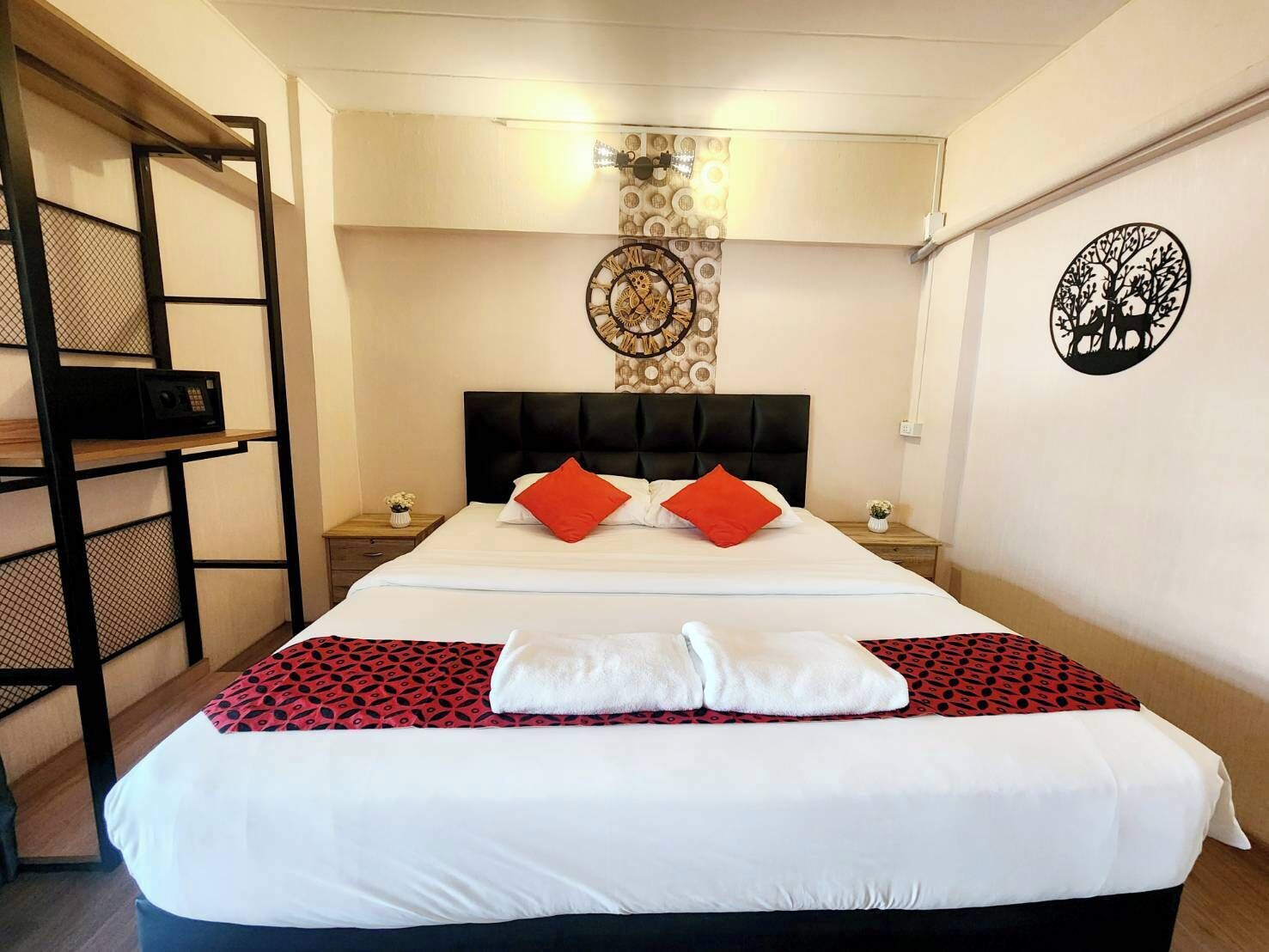 A hotel room with a large bed, two nightstands, a wall clock, and a decorative wall piece.