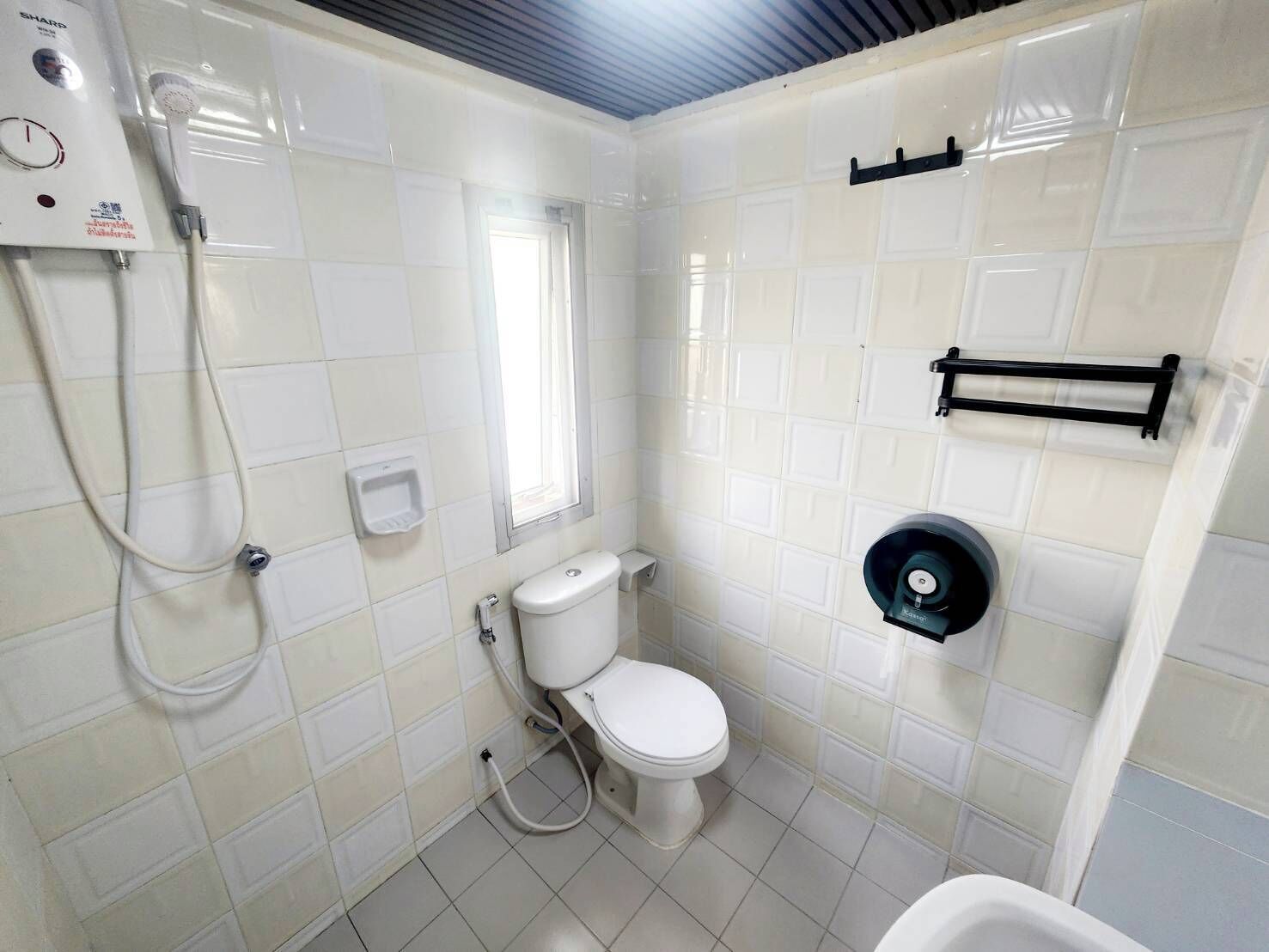 Un baño pequeño y limpio con azulejos blancos, un inodoro, ducha y secamanos.
