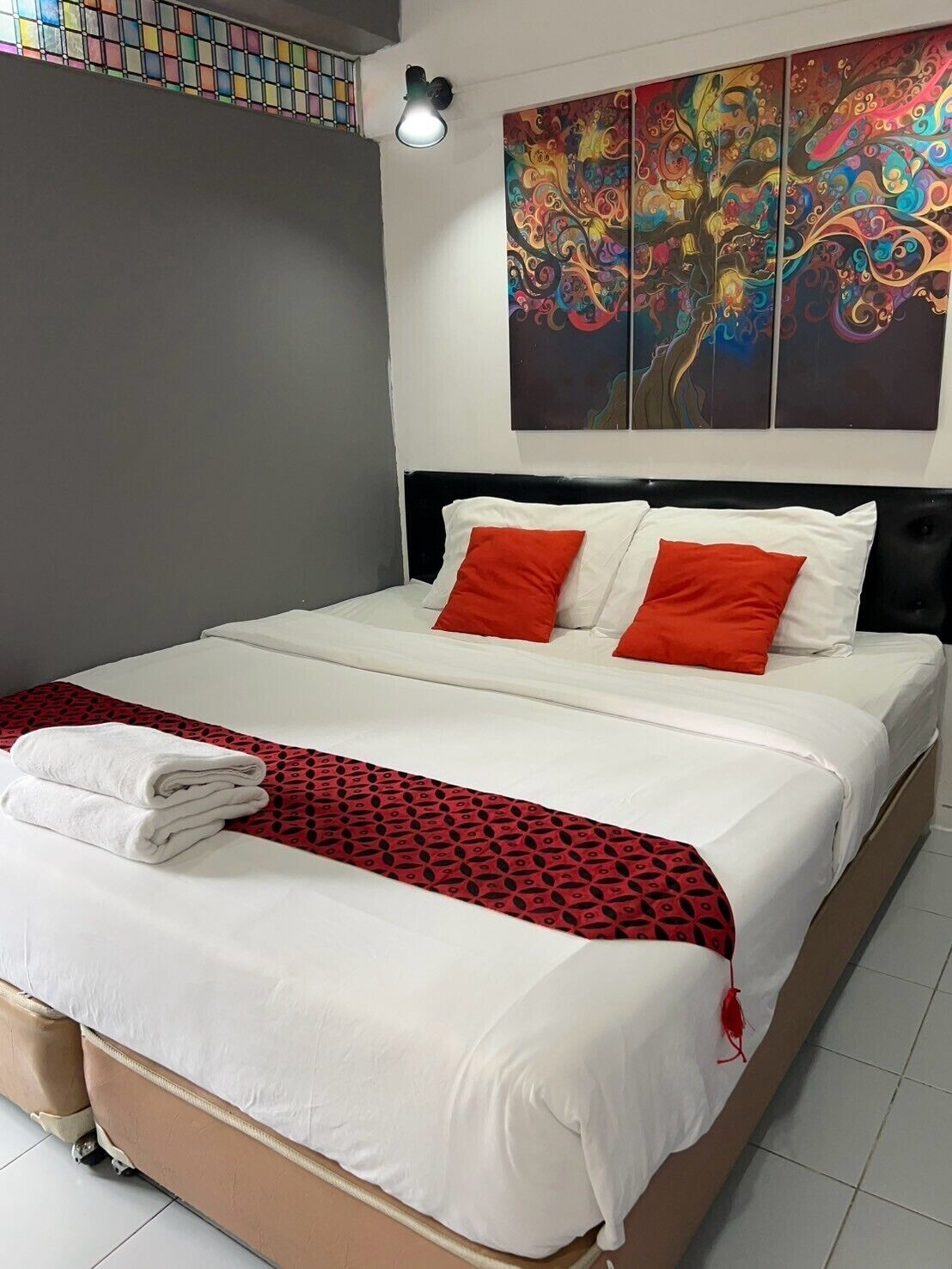 Una cama bien tendida con ropa de cama blanca y roja, un plaid rojo estampado y un par de toallas blancas.