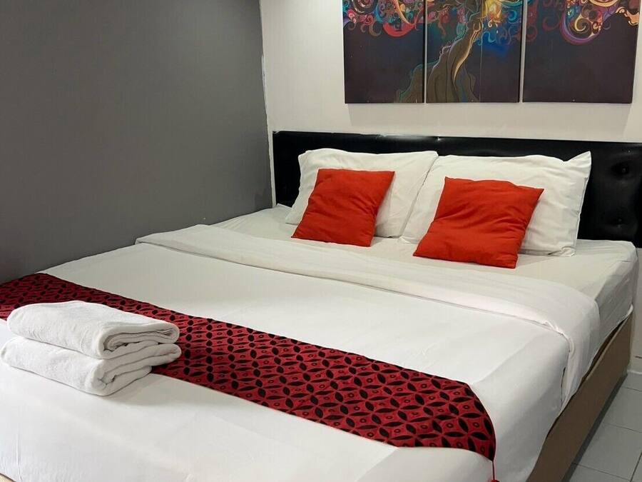 A neatly made bed with white and red bedding, a red patterned throw, and a pair of white towels.