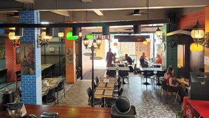 Un restaurante con paredes de ladrillo, piso de baldosas y faroles colgantes. Mesas y sillas dispuestas para comer.