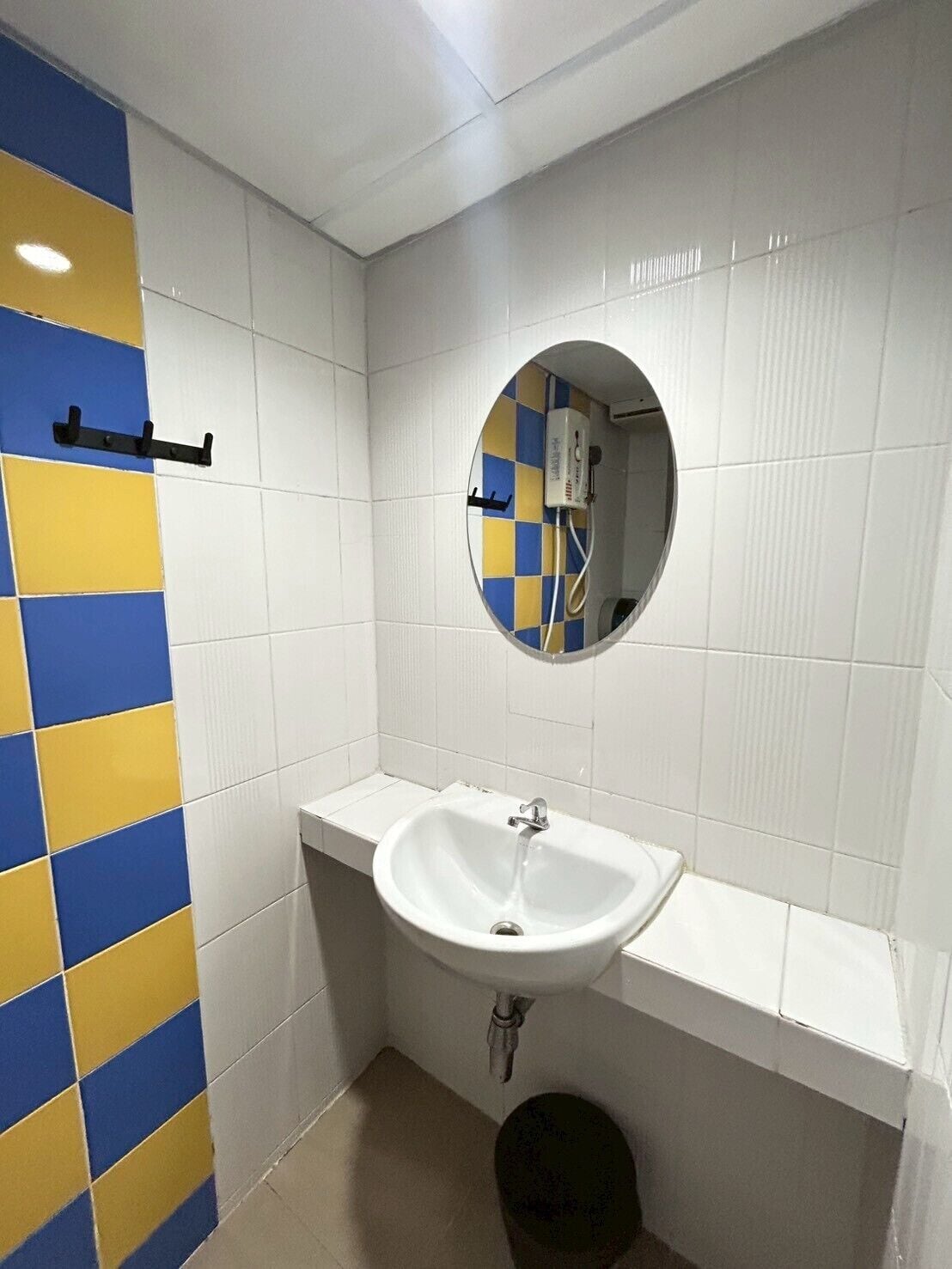 Un baño con un lavamanos blanco, un espejo y un inodoro. Las paredes están cubiertas de azulejos con un diseño azul y amarillo.
