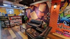 Zona de recepción con mostrador, un sofá de cuero negro, una mesita y una pared decorada con un mural colorido.