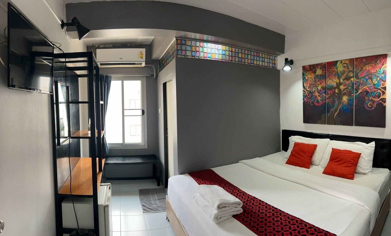 A modern hotel room with a bed, a bench, a TV, and a large window.